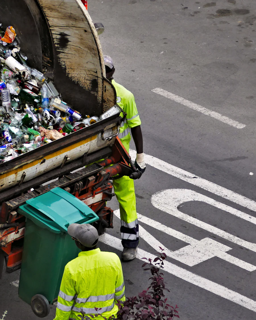 Collection crew in high-visibility clothing emptying a green bin into a refuse truck