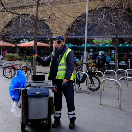 Street cleaner in a high-visibility vest with a cleaning cart