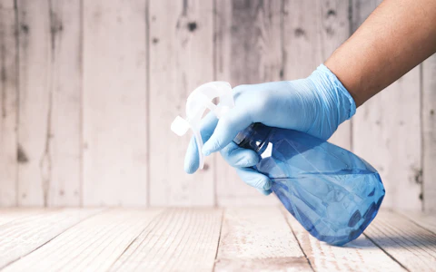 Gloved hand holding a blue spray bottle of cleaner