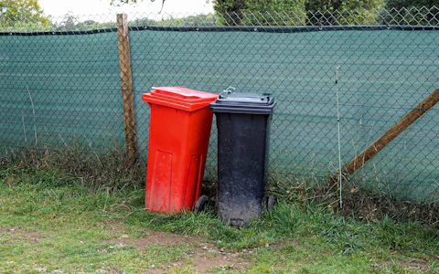 Red and black wheelie bins standing against a green mesh fence