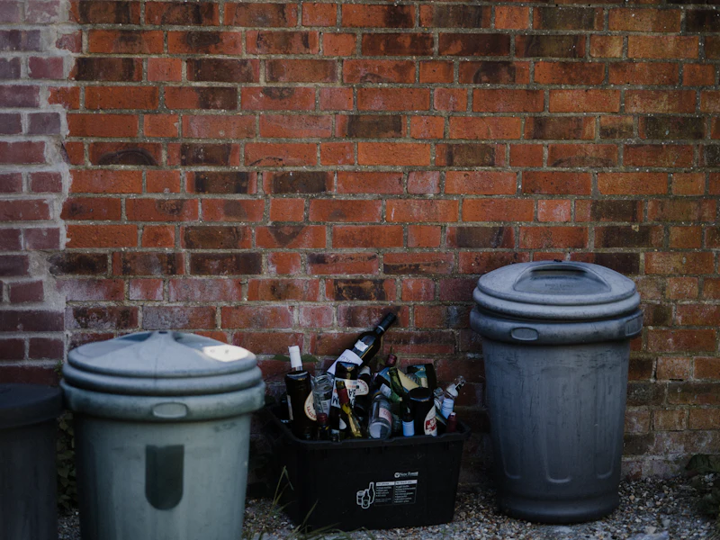 Household wheelie bins with closed lids lined up against a brick wall