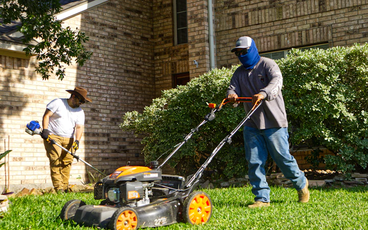 Two groundskeepers mowing and trimming a lawn