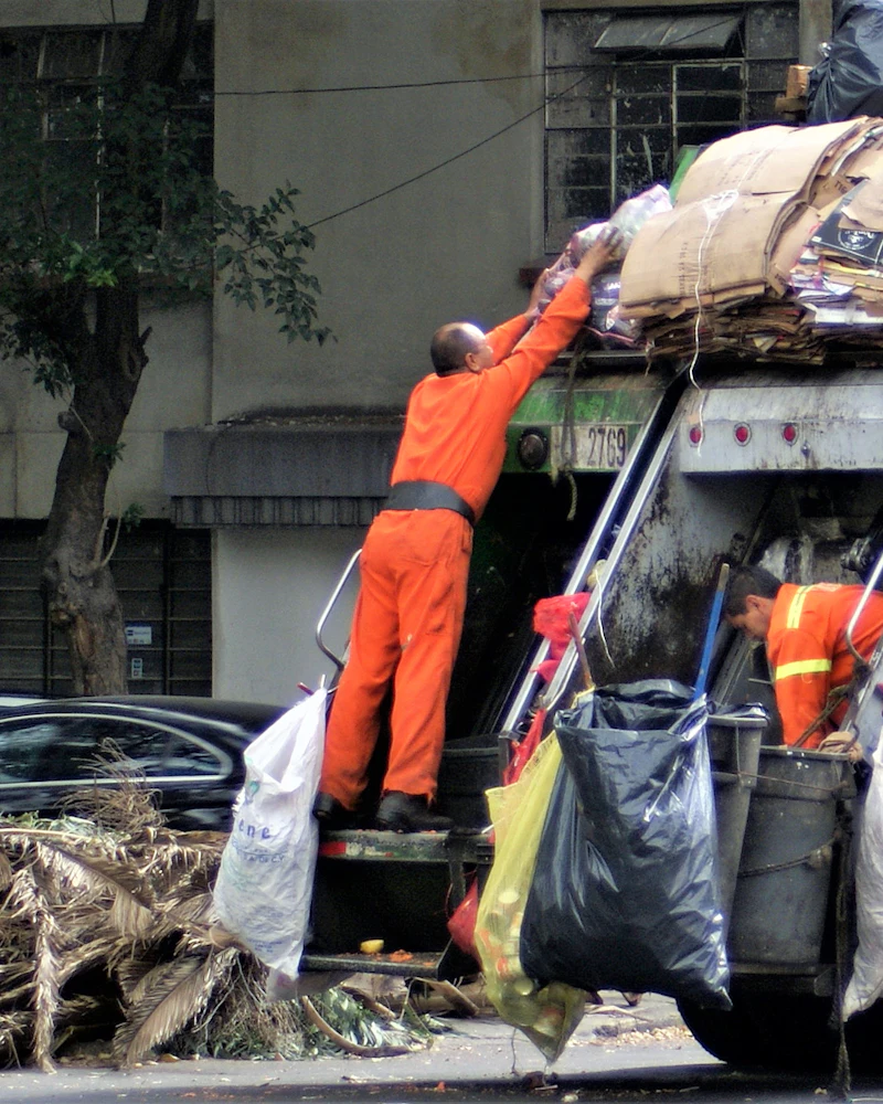 Waste operative in high-visibility clothing beside collected refuse sacks